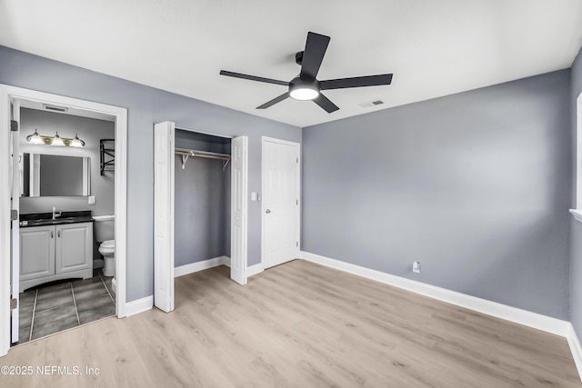 unfurnished bedroom with light wood-style flooring, visible vents, baseboards, a closet, and ensuite bath