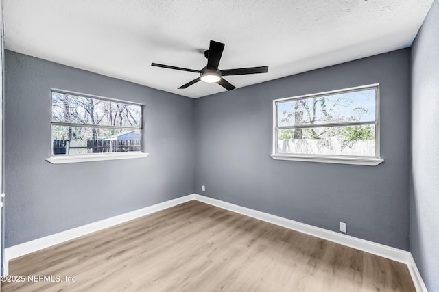 unfurnished room with ceiling fan, a textured ceiling, baseboards, and wood finished floors