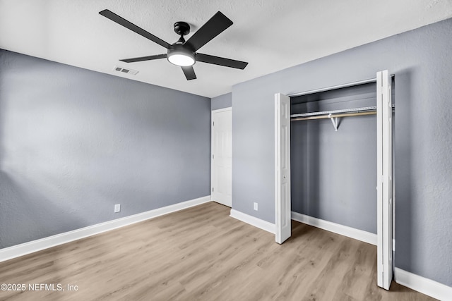 unfurnished bedroom featuring baseboards, visible vents, a ceiling fan, wood finished floors, and a closet