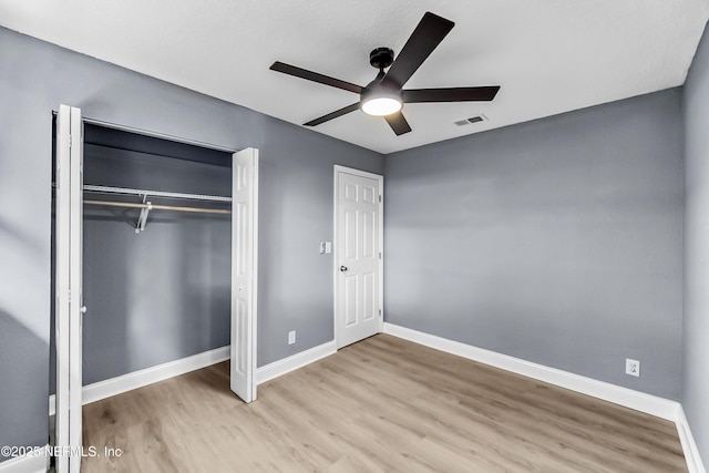 unfurnished bedroom with a closet, wood finished floors, visible vents, and baseboards