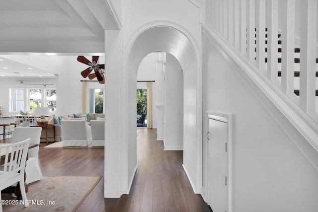 foyer entrance featuring arched walkways, baseboards, a ceiling fan, and dark wood-style flooring