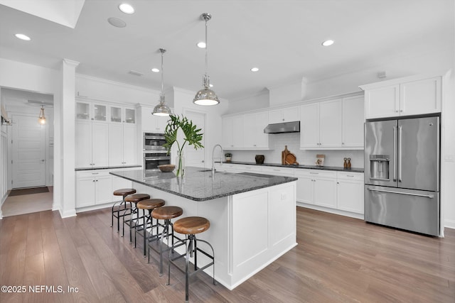 kitchen featuring backsplash, under cabinet range hood, stainless steel appliances, wood finished floors, and white cabinetry