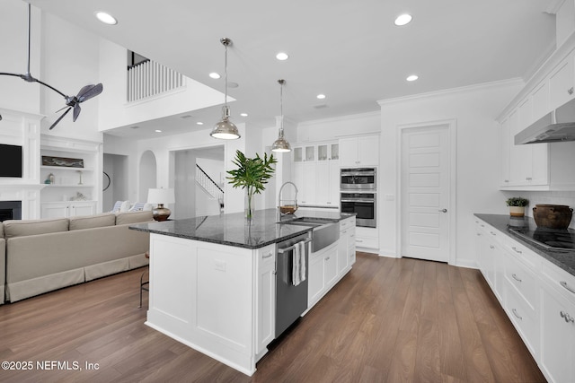 kitchen with dark wood finished floors, a kitchen island with sink, a sink, appliances with stainless steel finishes, and white cabinetry