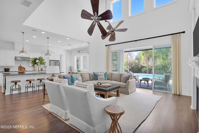 living room with visible vents, dark wood-type flooring, a towering ceiling, and a ceiling fan