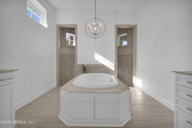 bathroom with a bath, a notable chandelier, vanity, and baseboards