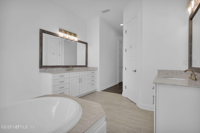 full bath with a bath, two vanities, baseboards, and a sink