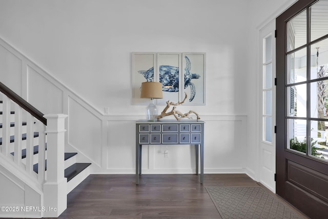 entryway with dark wood finished floors, stairway, and a decorative wall