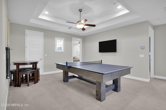 recreation room with a raised ceiling, light carpet, and ceiling fan