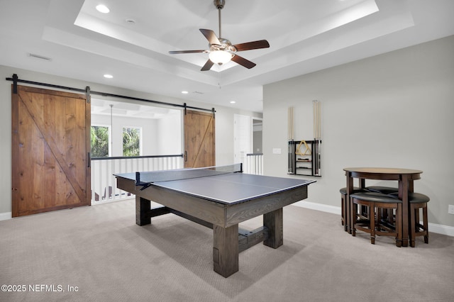 rec room with a tray ceiling, a barn door, and light carpet