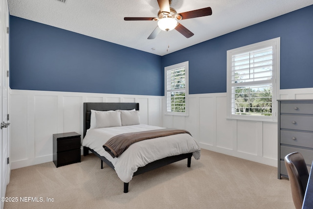 bedroom with light colored carpet, ceiling fan, wainscoting, and a textured ceiling