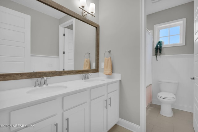 full bathroom featuring double vanity, toilet, a wainscoted wall, and a sink