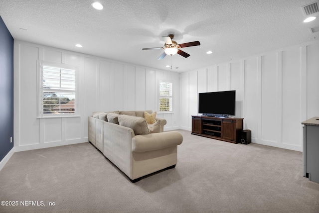 living room featuring a ceiling fan, a decorative wall, light colored carpet, and visible vents