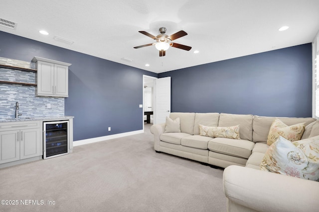 living area with visible vents, a ceiling fan, wine cooler, wet bar, and light colored carpet