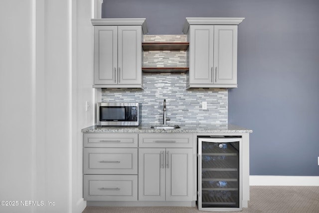 bar featuring beverage cooler, stainless steel microwave, backsplash, and a sink