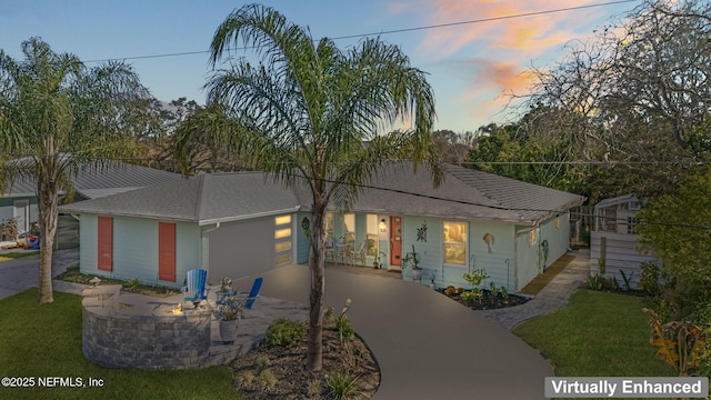 view of front of property featuring concrete driveway, roof with shingles, a patio area, and a lawn