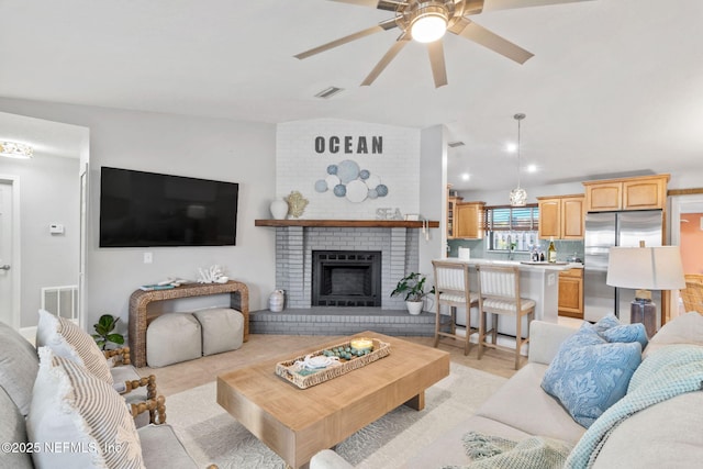 living area featuring vaulted ceiling, ceiling fan, a fireplace, and visible vents