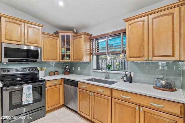 kitchen with light stone counters, backsplash, appliances with stainless steel finishes, glass insert cabinets, and a sink