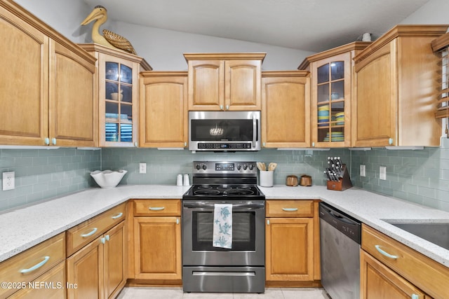 kitchen featuring stainless steel appliances, vaulted ceiling, backsplash, light stone countertops, and glass insert cabinets