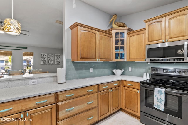 kitchen with glass insert cabinets, appliances with stainless steel finishes, backsplash, and light stone counters