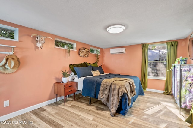 bedroom featuring light wood-style floors, baseboards, a textured ceiling, and a wall mounted AC