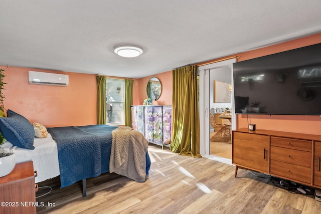 bedroom with a textured ceiling, a wall mounted AC, and light wood-type flooring