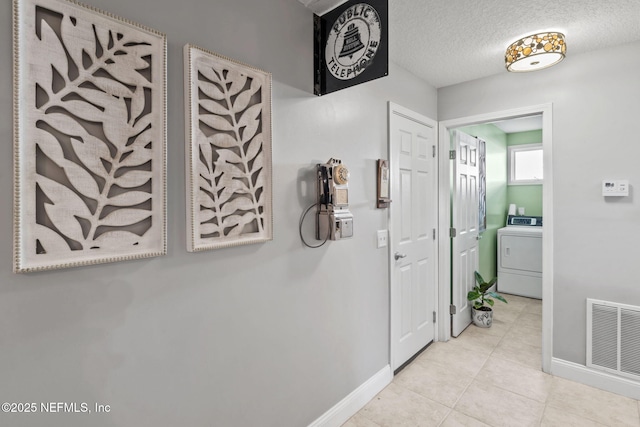 hall featuring a textured ceiling, tile patterned flooring, visible vents, baseboards, and washer / dryer