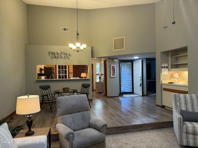 living area with a chandelier, a towering ceiling, wood finished floors, and visible vents