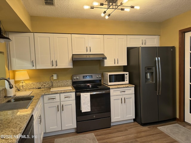 kitchen with appliances with stainless steel finishes, wood finished floors, under cabinet range hood, white cabinetry, and a sink