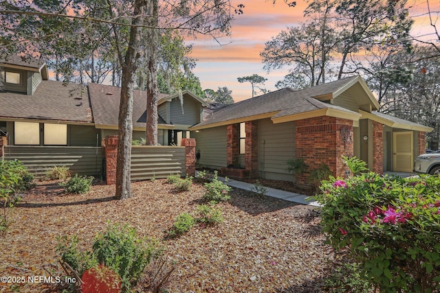 exterior space featuring brick siding, roof with shingles, and fence