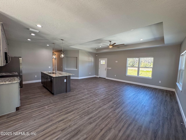 kitchen featuring baseboards, appliances with stainless steel finishes, dark wood-style floors, a tray ceiling, and a center island with sink