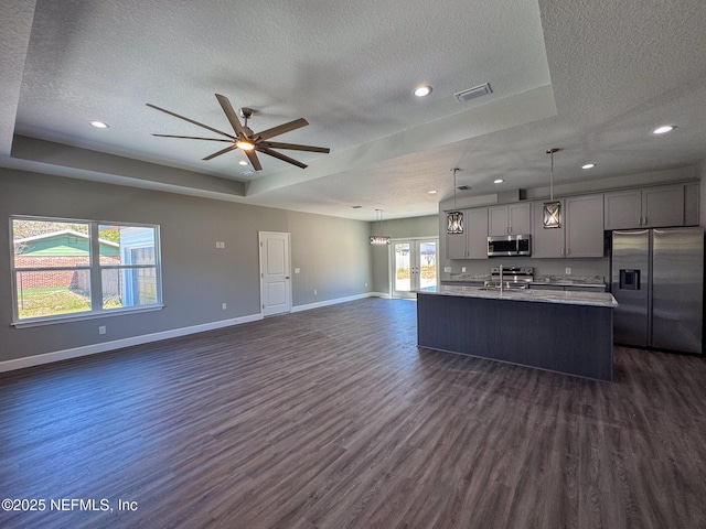 kitchen featuring visible vents, open floor plan, a tray ceiling, stainless steel appliances, and gray cabinetry