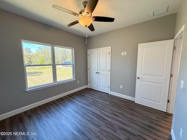 unfurnished bedroom featuring visible vents, dark wood finished floors, a textured ceiling, and baseboards