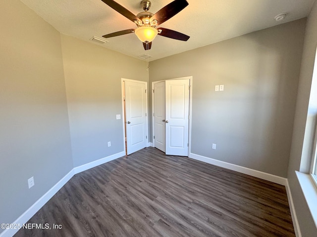 unfurnished bedroom with dark wood-style floors, a ceiling fan, visible vents, and baseboards