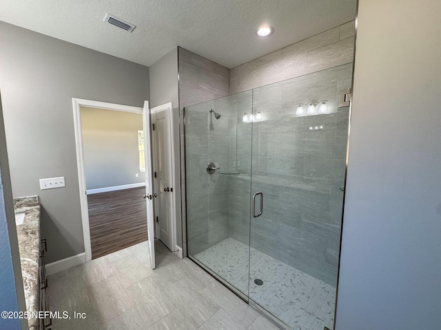 full bath featuring a stall shower, visible vents, a textured ceiling, and baseboards