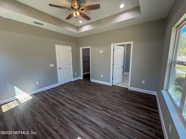 unfurnished bedroom with a tray ceiling, dark wood-style flooring, visible vents, and baseboards