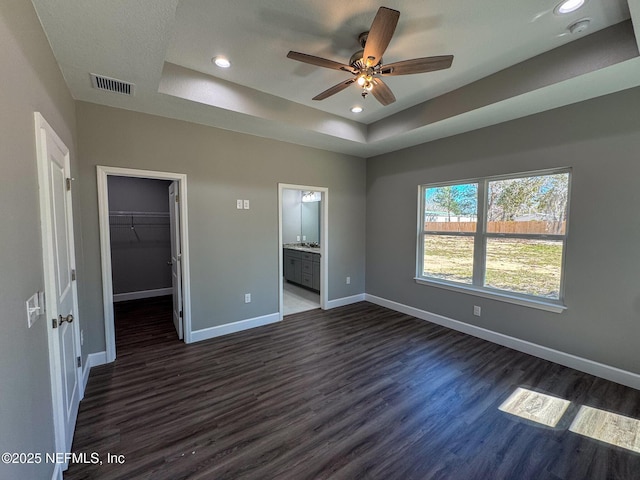 unfurnished bedroom with a walk in closet, dark wood finished floors, a raised ceiling, visible vents, and baseboards