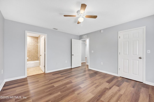 unfurnished bedroom featuring ensuite bath, wood finished floors, visible vents, and baseboards