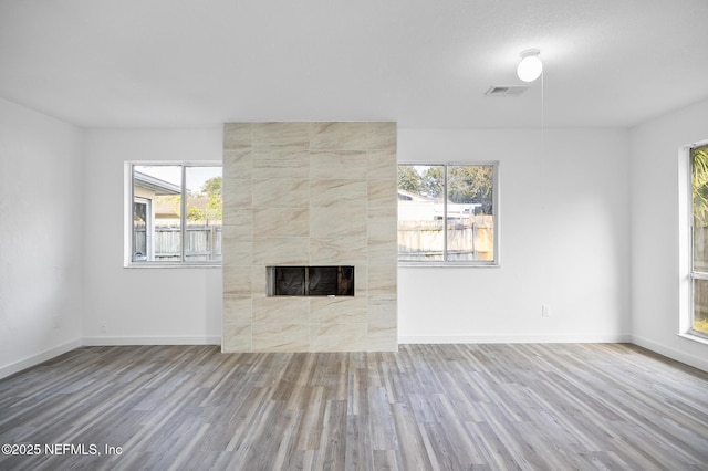 unfurnished living room featuring a tiled fireplace, wood finished floors, visible vents, and baseboards