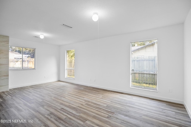 unfurnished room with a wealth of natural light, visible vents, baseboards, and wood finished floors