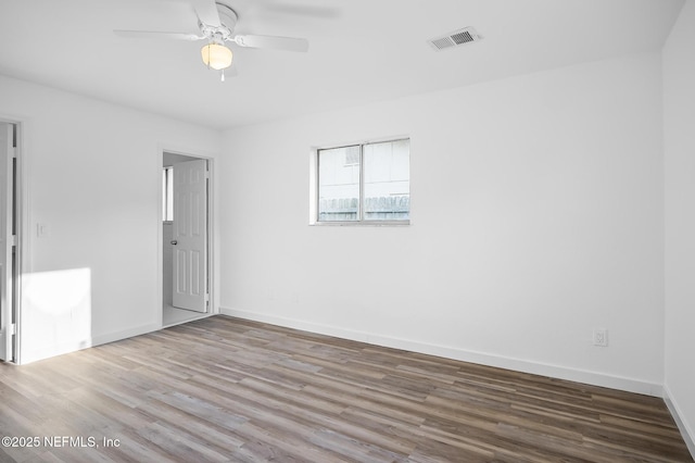 empty room featuring a ceiling fan, wood finished floors, visible vents, and baseboards