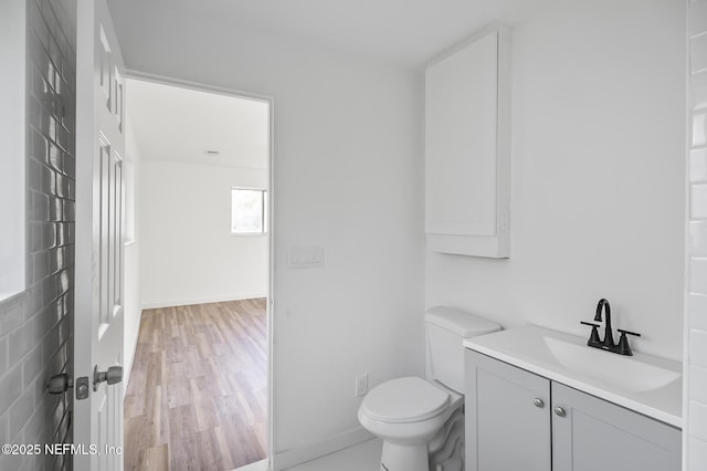 half bath with vanity, toilet, wood finished floors, and baseboards