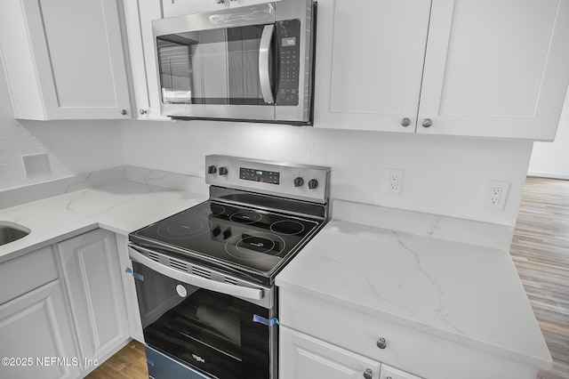 kitchen featuring white cabinets, appliances with stainless steel finishes, light wood-style floors, and light stone countertops