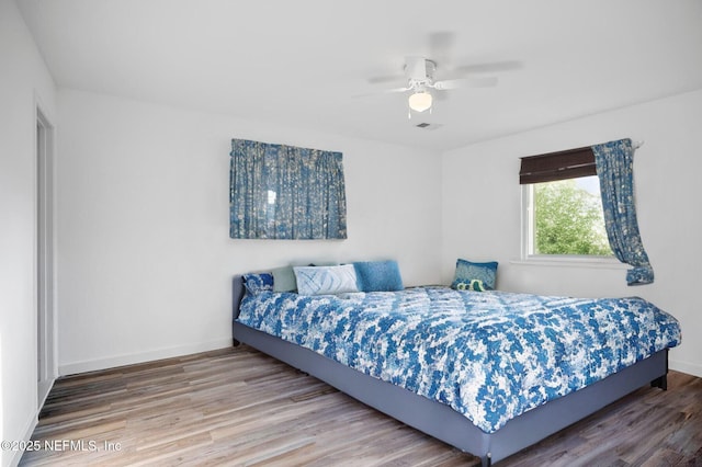 bedroom featuring visible vents, a ceiling fan, baseboards, and wood finished floors