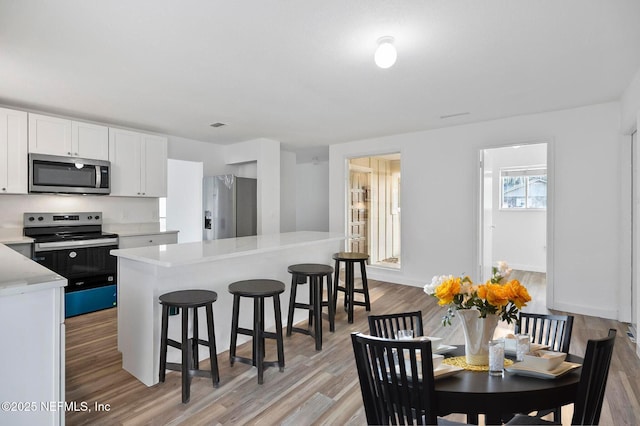 kitchen with light wood-type flooring, white cabinetry, appliances with stainless steel finishes, a breakfast bar area, and light countertops