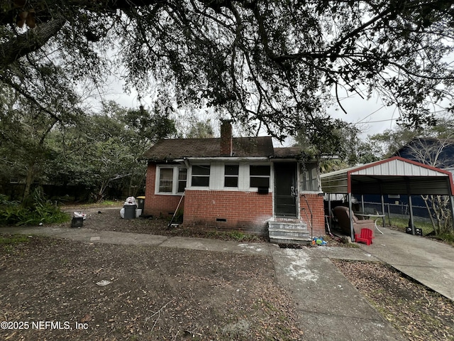 bungalow-style house with brick siding, driveway, crawl space, a carport, and a chimney