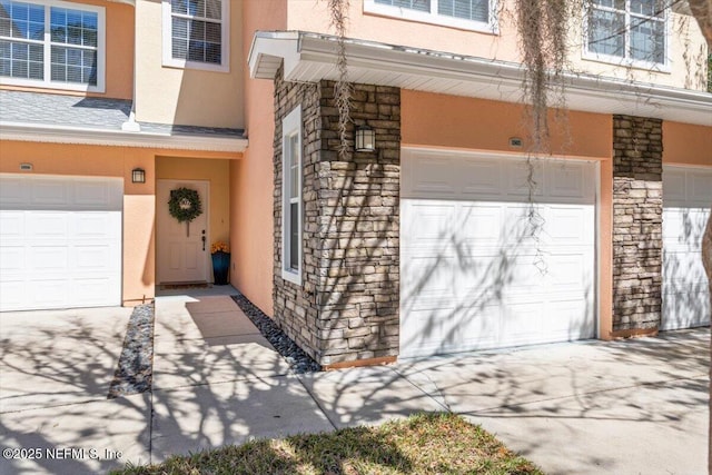 entrance to property with a garage, stone siding, concrete driveway, and stucco siding