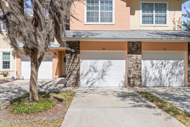 view of front of property with a garage, concrete driveway, stone siding, and stucco siding