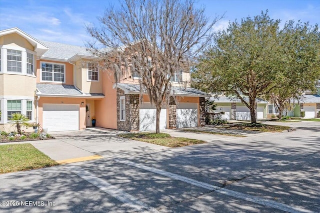 multi unit property with stone siding, driveway, an attached garage, and stucco siding