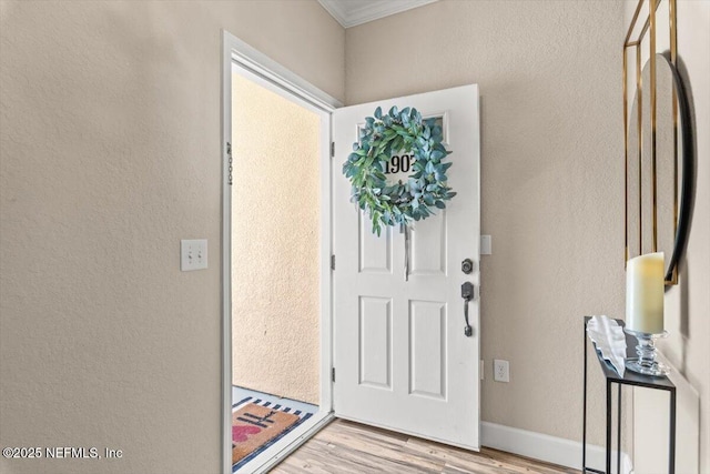 entrance foyer with light wood-style floors, a textured wall, crown molding, and baseboards