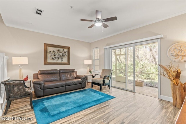 living room with ceiling fan, light wood-style flooring, visible vents, baseboards, and ornamental molding